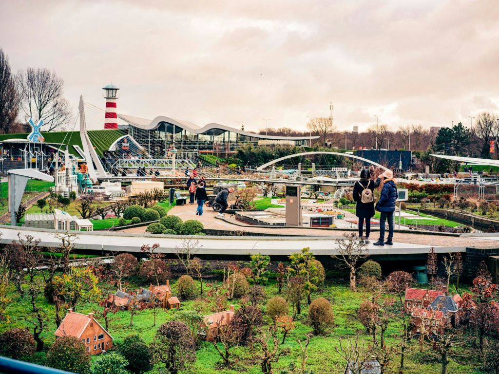 녹음이 우거진 단풍, 미니어처 건물, 등대가 있는 공원 같은 지역에 사는 사람들. 보행자가 있는 통로가 보입니다.