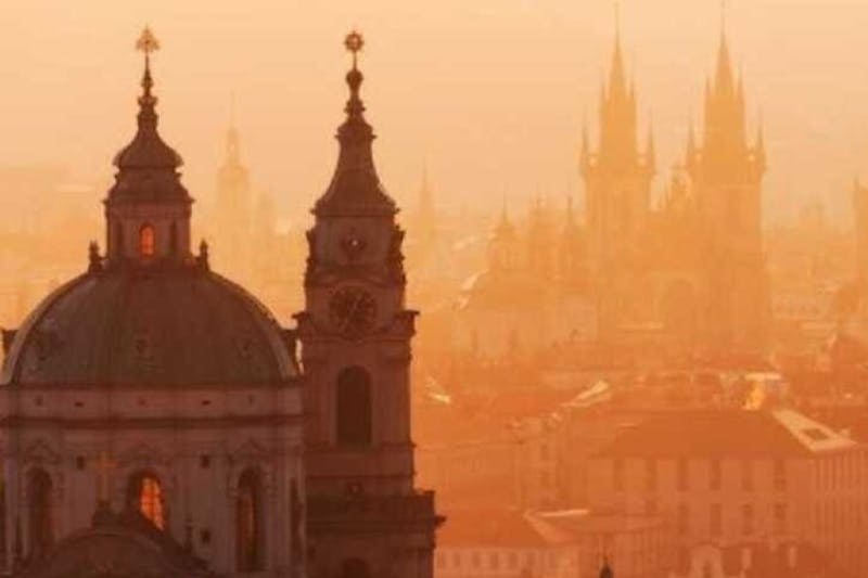 도시 건물을 배경으로 따뜻하고 주황색의 석양을 배경으로 화려한 타워와 첨탑의 실루엣이 펼쳐집니다.