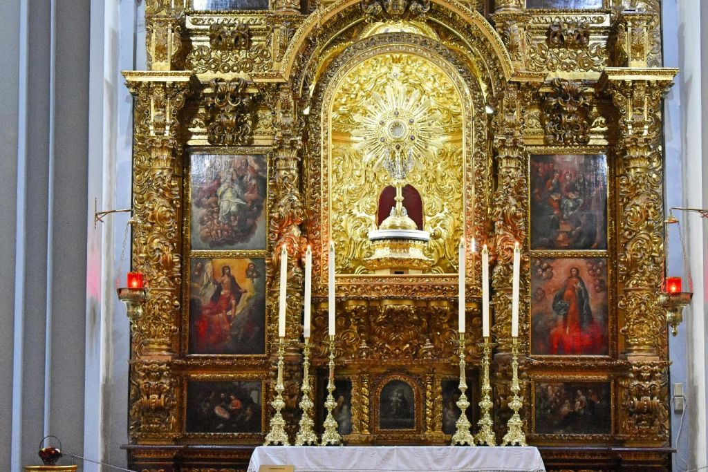 종교적인 그림, 6개의 높은 촛대, 정교하게 디테일한 햇살로 장식된 화려하고 금빛 제단화.