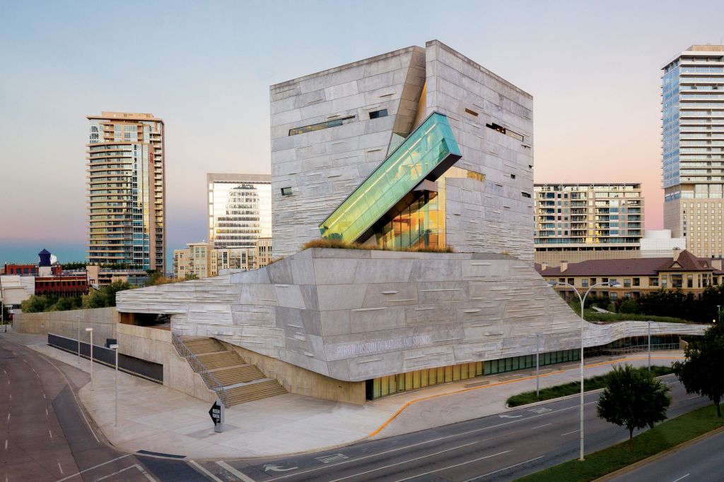 고층 건물의 도시 배경을 배경으로 각진 콘크리트 구조와 유리 연장으로 꾸며진 현대적인 건물.