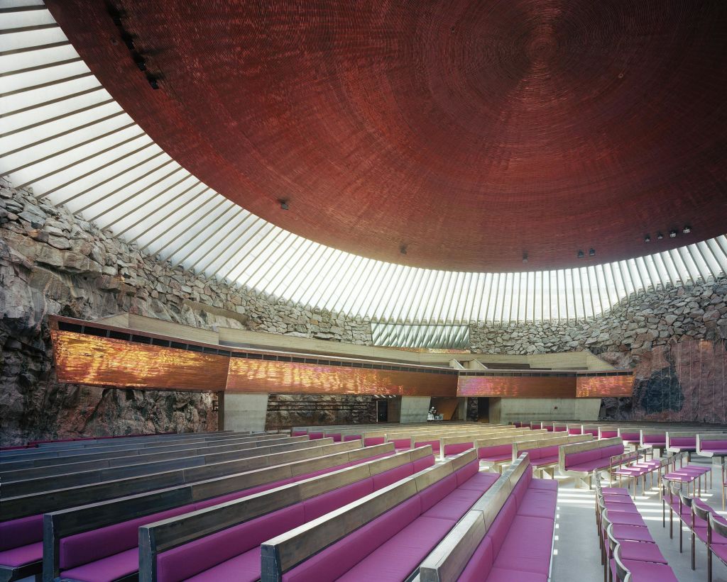 원형의 원목 질감의 천장, 유리 벽, 암석 지층, 보라색 쿠션 페우가 줄지어 있는 넓은 객실입니다.