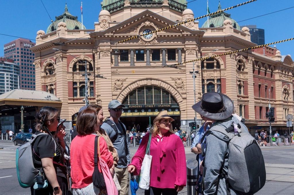 호주 멜버른의 유서 깊은 건물인 플린더스 스트리트 역 앞에 캐주얼한 복장을 한 사람들이 서 있습니다.