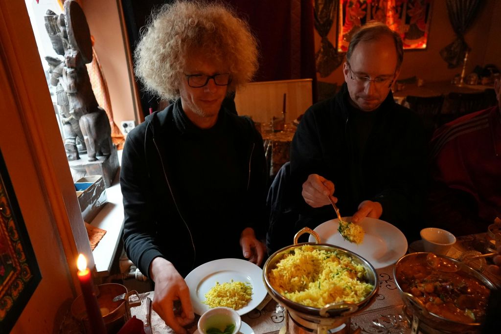 두 남자가 테이블에 앉아 노란 쌀과 카레의 공동 요리를 제공합니다.