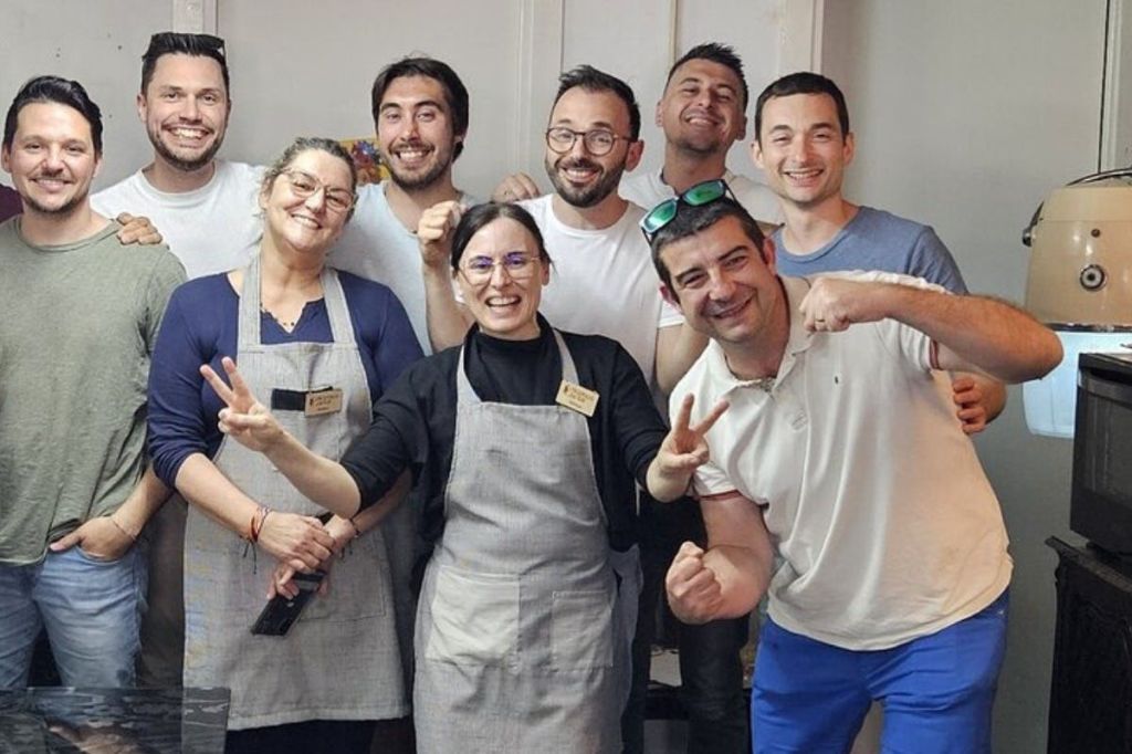 8명의 사람들이 웃고 있으며, 일부는 앞치마를 두르고 실내에서 함께 포즈를 취하고 있습니다. 두 사람이 평화 표지판을 들고 있습니다.