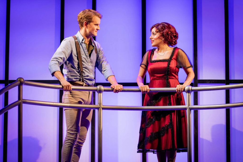 두 배우가 파란색 배경의 발코니에 서서 대화를 나누고 있습니다.