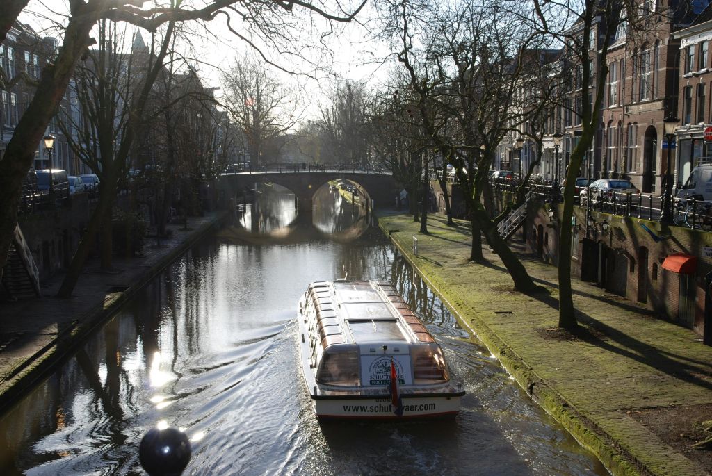 운하 보트가 나무가 늘어선 수로를 지나 화창한 날 돌다리를 향해 항해합니다.