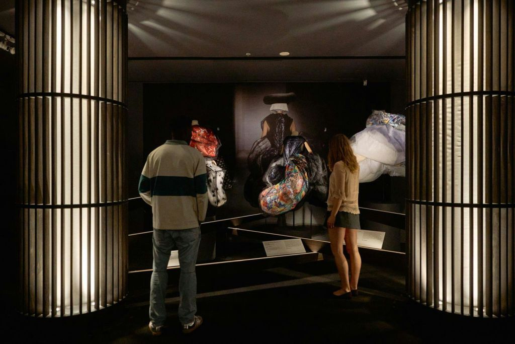 조명이 어두운 방에서 초점 조명 아래 다채롭고 추상적인 조각품을 전시하는 박물관을 관찰하는 두 사람.