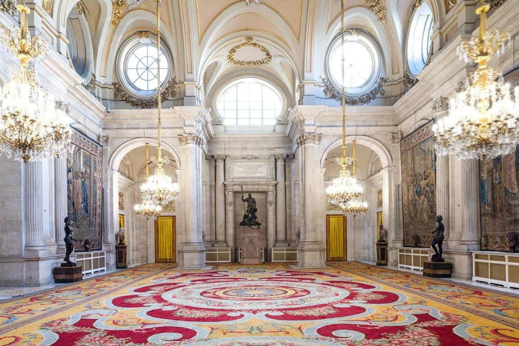 화려한 샹들리에, 아치형 창문, 조각상, 장식용 태피스트리, 활기찬 패턴의 카펫이 있는 그랜드 홀.