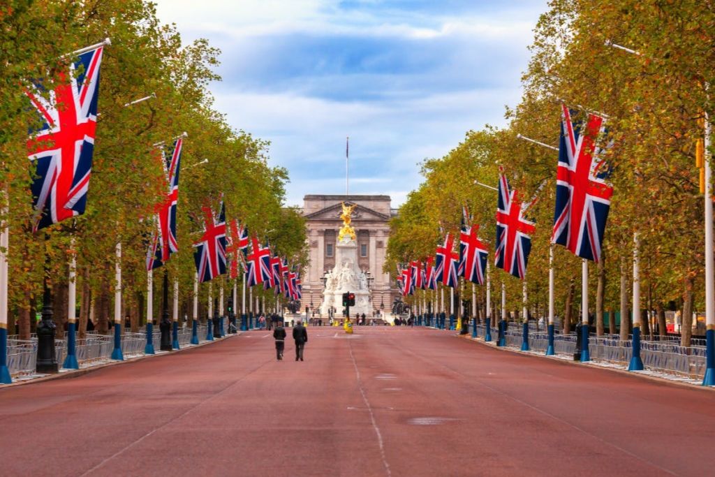 영국 국기와 나무가 늘어선 넓은 거리를 배경으로 기념비와 커다란 유서 깊은 건물이 나옵니다.