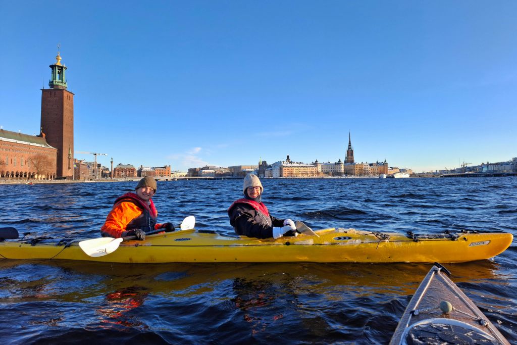 도시의 스카이라인과 맑고 푸른 하늘을 배경으로 강에서 겨울 카약을 타는 두 사람.
