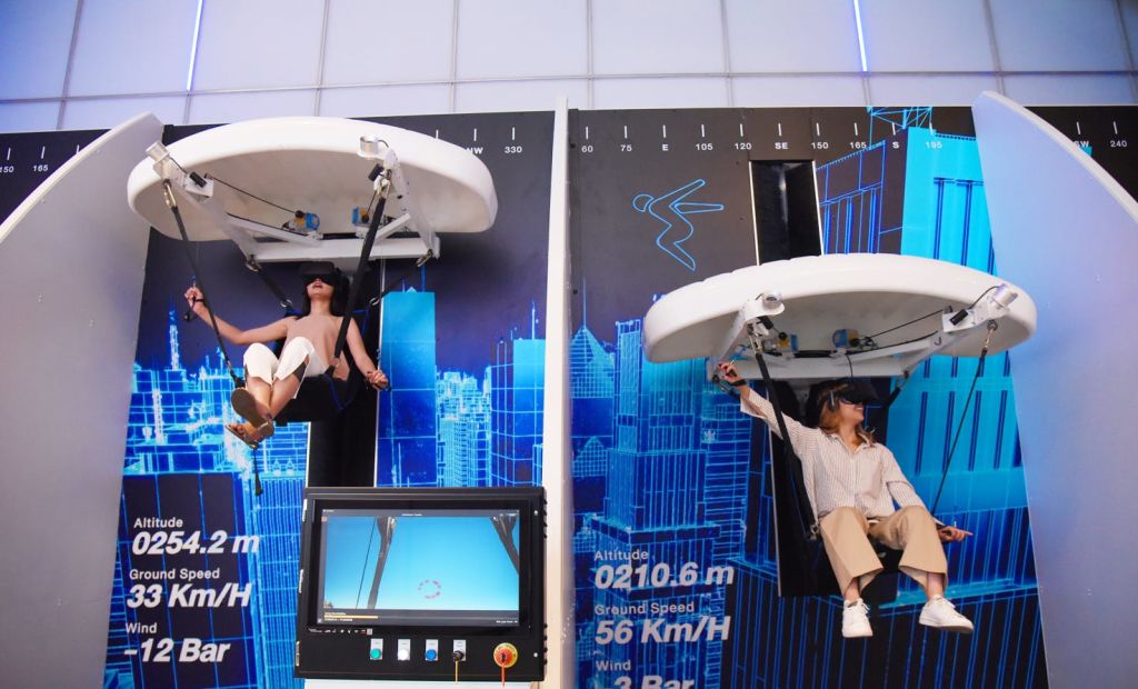 두 사람이 가상 현실에 앉아 푸른 도시 풍경을 배경으로 활공 시뮬레이터를 매달고 지표가 표시됩니다.