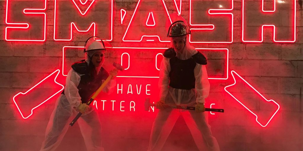 보호구와 헬멧을 쓴 두 사람이 붉은 네온사인과 연기가 자욱한 배경 앞에서 썰매 해머를 들고 있습니다.