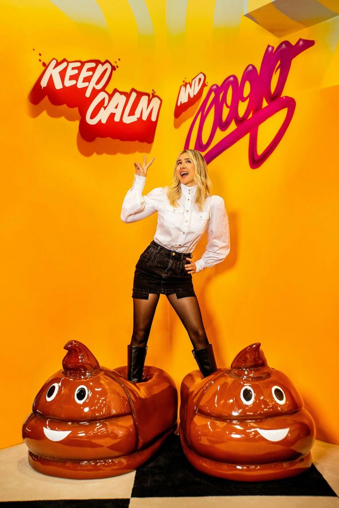빨간색과 보라색 레터링으로 된 "KEEP CALM AND 10000" 문구가 있는 밝은 노란색 배경 앞에서 미소 짓는 여성이 포즈를 취하고 있습니다.