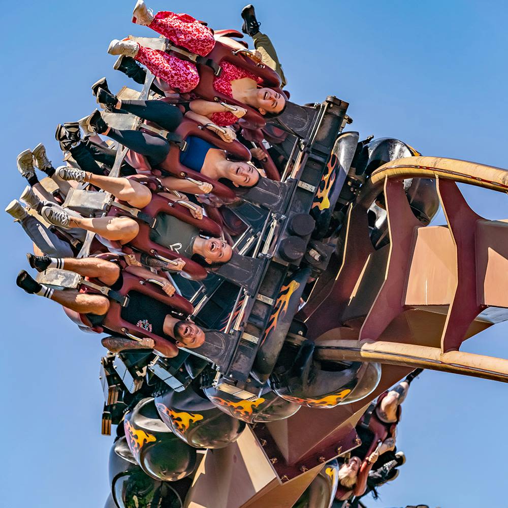 거꾸로 된 롤러코스터를 타는 사람들은 맑고 푸른 하늘을 배경으로 흥분과 두려움의 표정으로 핸들바를 단단히 움켜쥐고 있습니다.