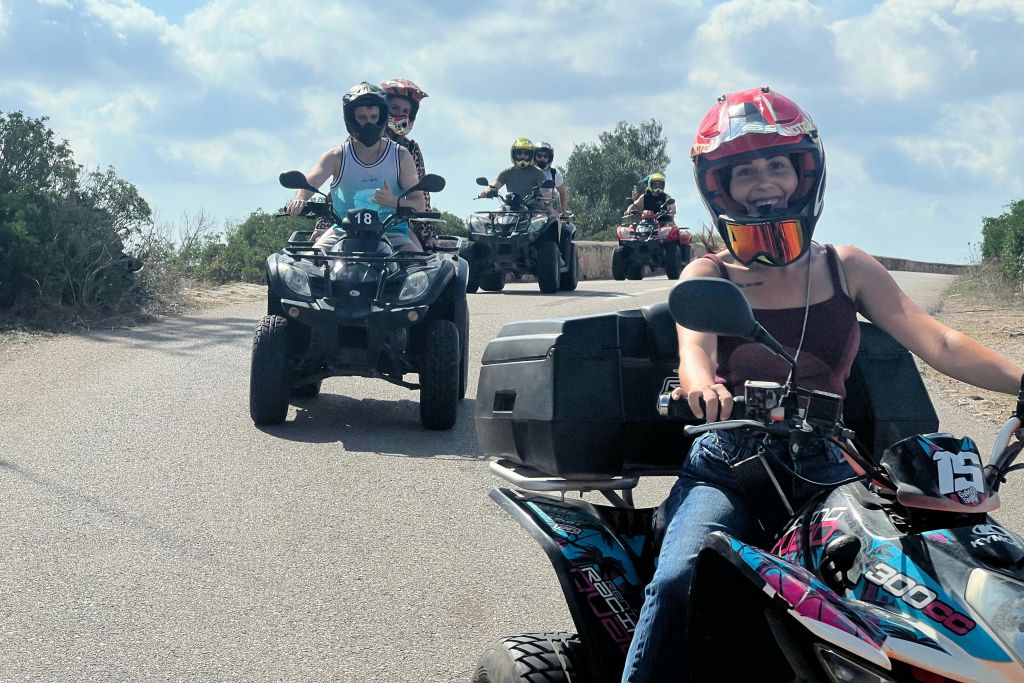 도로에서 ATV를 타는 사람들의 그룹. 앞에 있던 사람이 빨간 헬멧과 검은색 탱크탑을 착용하고 미소를 짓고 있습니다.