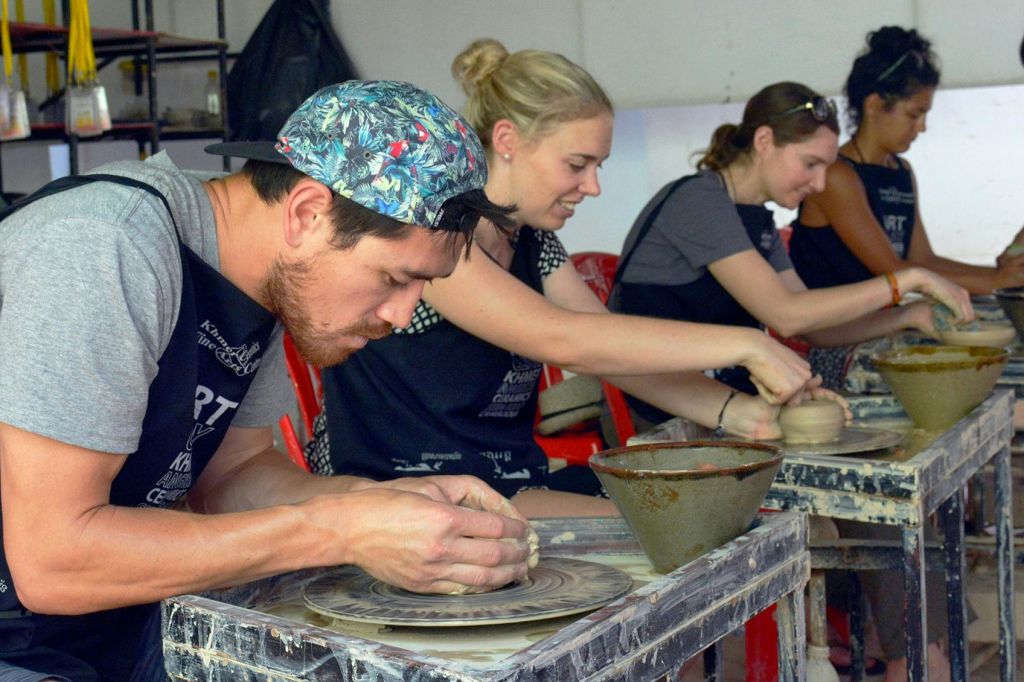 도자기 제작에 종사하는 한 무리의 사람들이 공방에 앉아 회전 바퀴로 점토를 만듭니다.