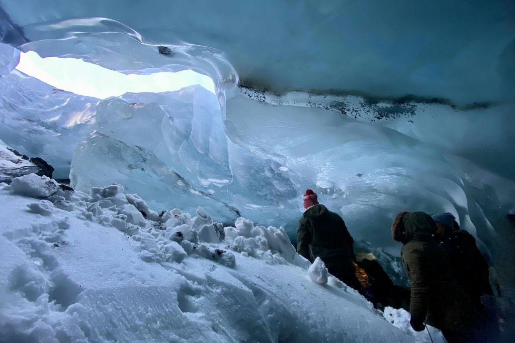 겨울 옷을 입은 두 사람이 푸른 얼음 동굴 안을 탐험하고 눈과 얼음이 둘러싸고 있습니다.