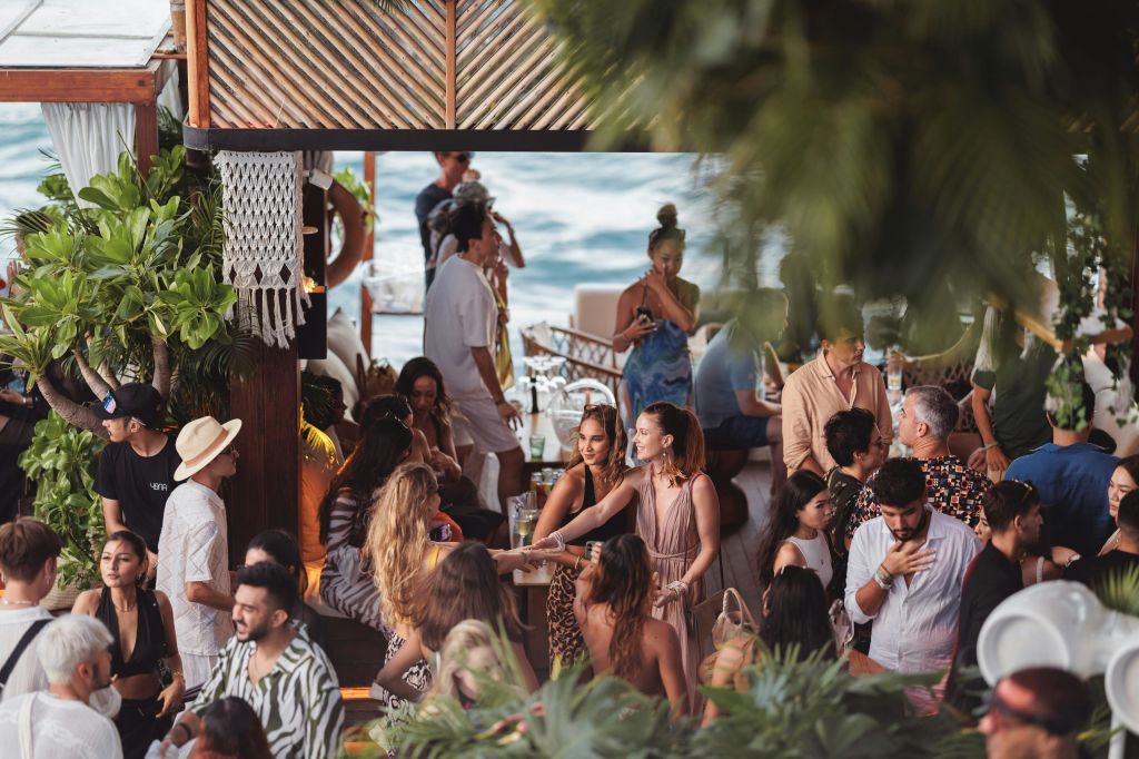 푸르름과 바다 전망을 배경으로 테이블과 바에서 사람들과 어울리는 활기찬 해변 모임.