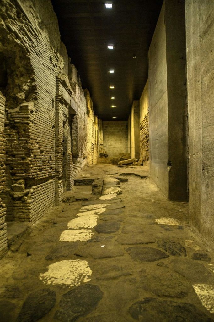 풍화 된 벽돌 벽, 부분적으로 손상되지 않은 아치, 고르지 않은 돌 바닥이있는 고대의 희미한 석재 복도.