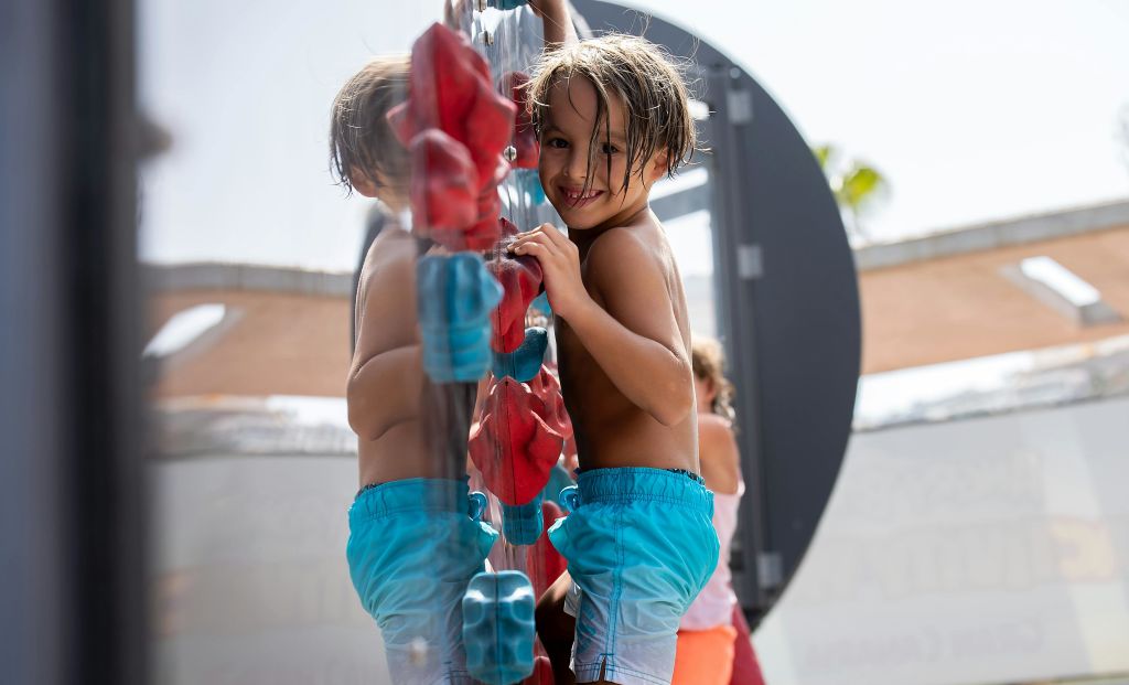 파란색 반바지를 입은 어린이가 놀이터 구조물에 올라가 카메라를 향해 미소를 짓고 다른 어린이를 배경으로 합니다.