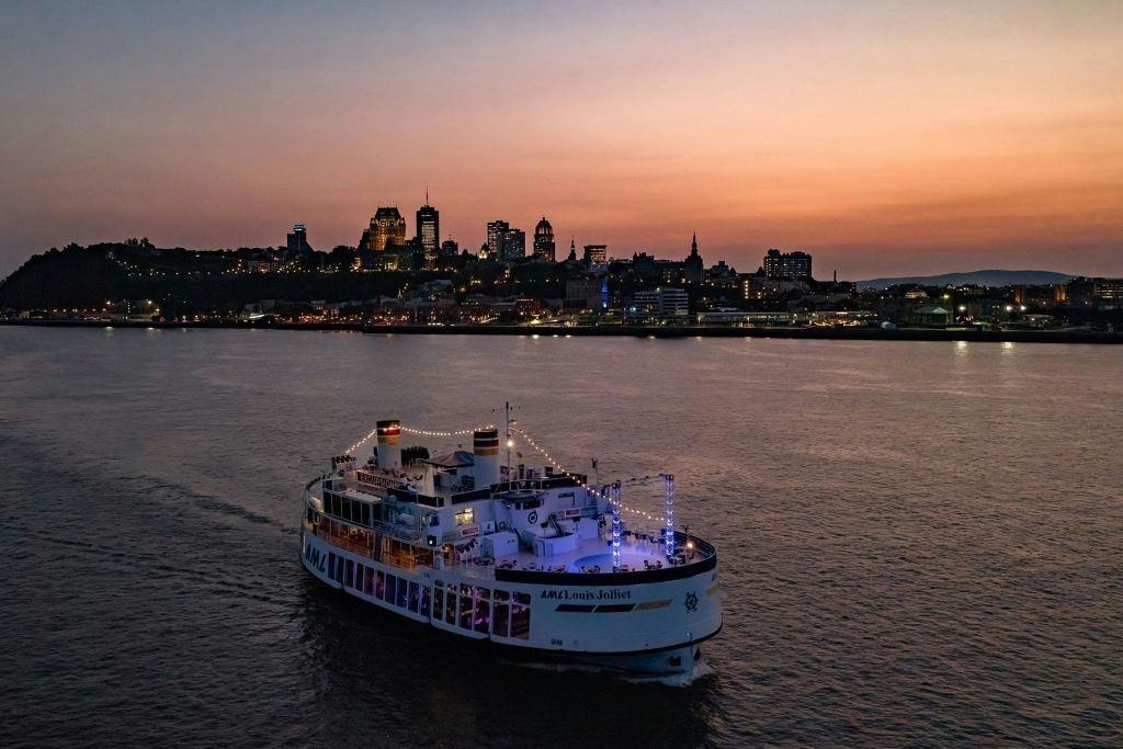 해질 무렵 강에서 항해하는 페리로, 도시의 스카이라인을 배경으로 조명이 켜진 건물이 있습니다.