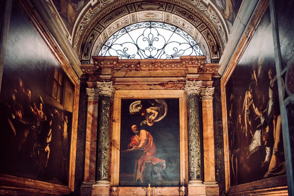 대리석 기둥과 정교한 천장 디테일이 장식된 커다란 종교 장면 그림이 있는 화려한 예배당 내부.