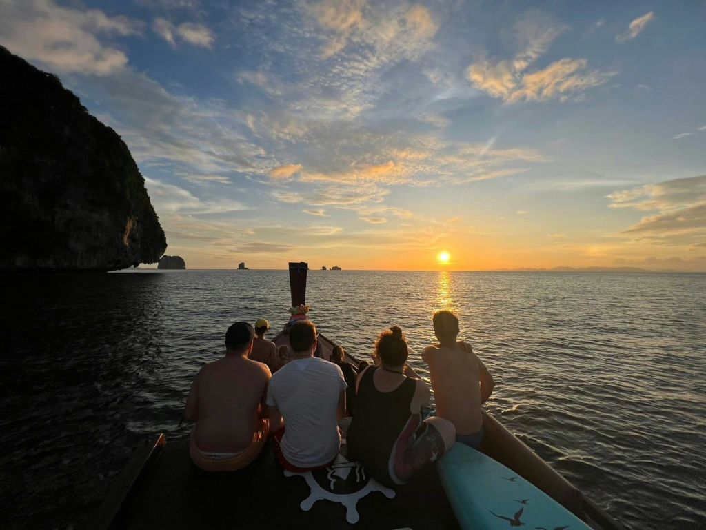 멀리 섬이 보이는 잔잔한 바닷가에서 일몰을 바라보는 보트에 다섯 명이 앉아 있습니다.