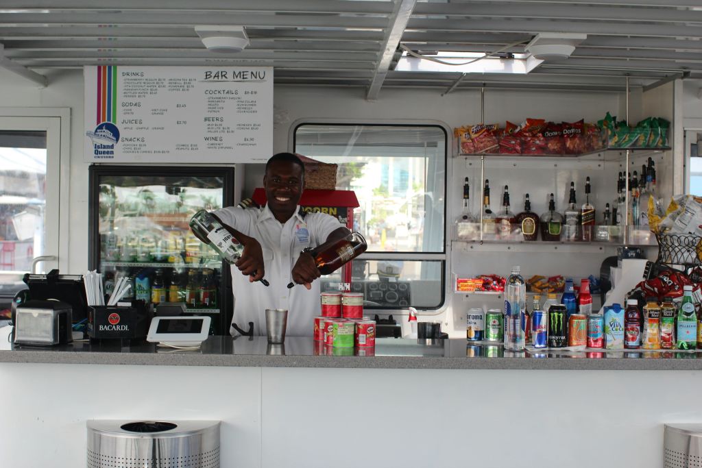 유니폼을 입은 남성은 간식, 병, 메뉴가 진열된 바 카운터에서 음료를 마십니다.