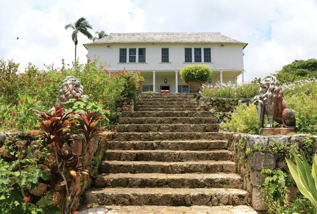 석조 계단을 올라가면 푸른색 셔터가 달린 2층짜리 하얀 집이 나오며, 울창한 녹음과 조각상으로 둘러싸여 있습니다.