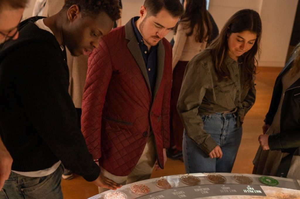 조명이 밝은 실내 환경에서 다양한 라벨 섹션이 있는 원형 디스플레이 테이블 주위에 서 있는 사람들의 그룹.