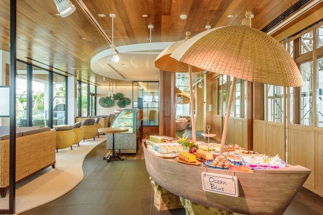 '오션 블루' 라고 적힌 나무 보트 모양의 뷔페 스테이션, 고리버들 가구, 커다란 창문이 특징인 레스토랑 인테리어.