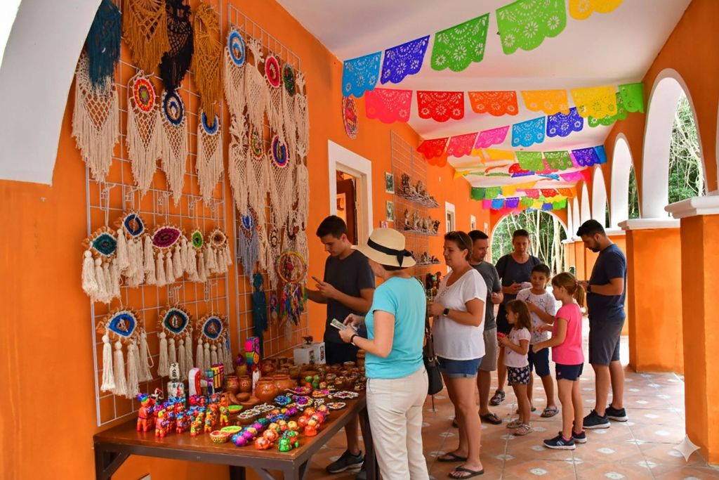 화려한 파펠 피카도 배너가 있는 장식된 복도 아래에서 다채로운 공예품과 기념품을 둘러보는 사람들.