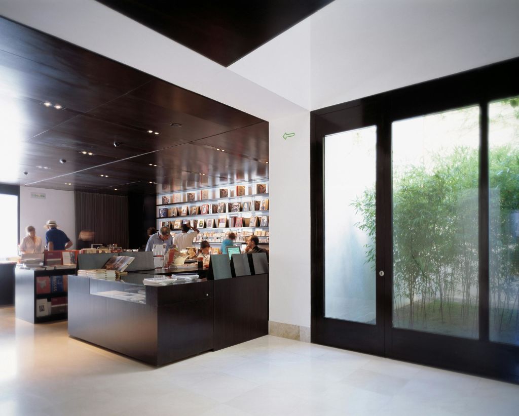 어두운 나무 선반, 전시된 책, 카운터, 야외 식물이 보이는 대형 유리문이 있는 현대적인 서점 내부.