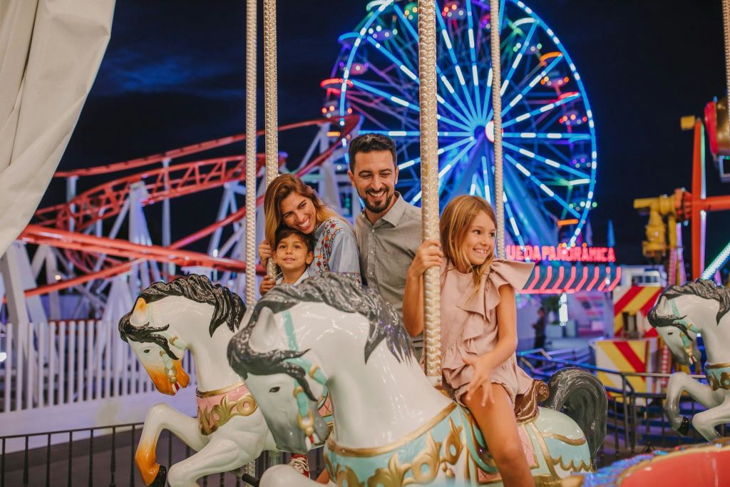 대관람차와 롤러코스터를 배경으로 야간에 회전목마를 타는 가족.