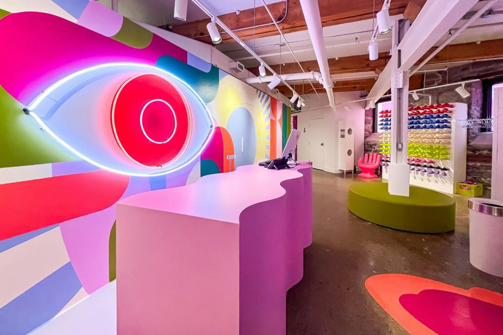 밝은 색상의 인테리어, 핑크색 물결 모양의 책상, 네온 아이 디자인, 생동감 넘치는 인테리어, 현대적인 가구와 디스플레이.