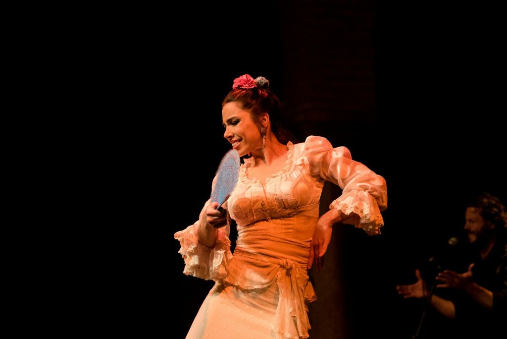 파란색 부채를 들고 있는 전통 드레스를 입은 여성이 극적인 조명 아래 무대에서 열정적으로 춤을 추고 있습니다.