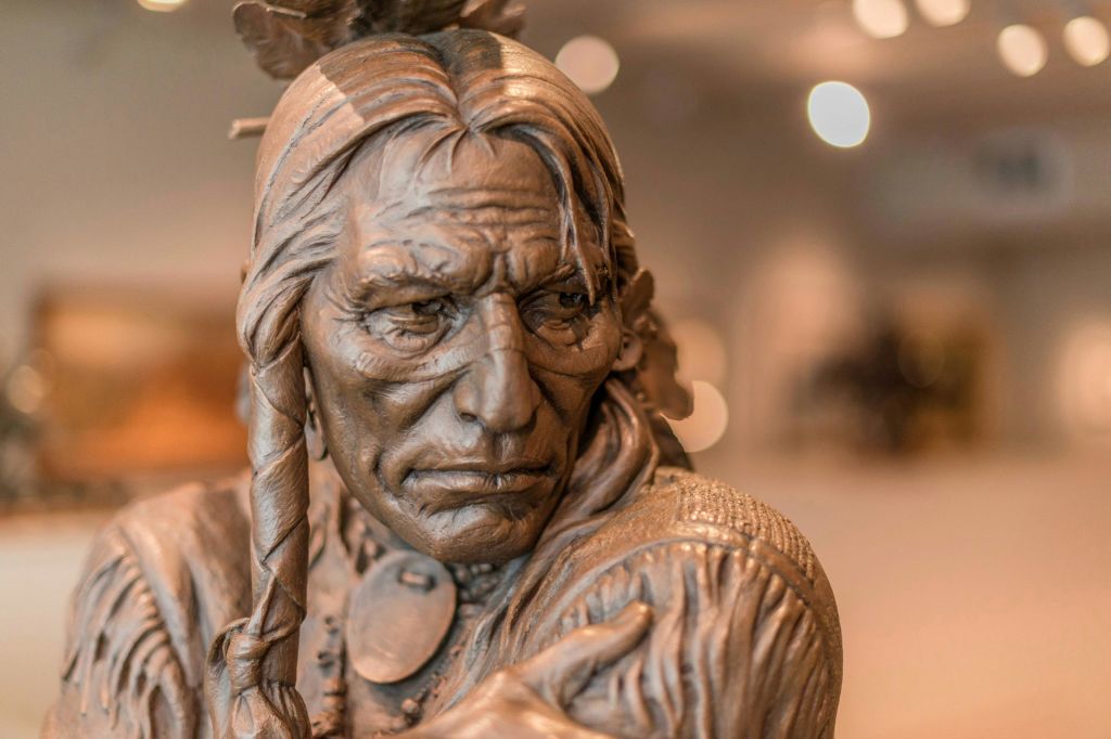 박물관에서 긴 머리카락, 땋은 가닥, 상세한 얼굴 특징을 가진 남자의 청동 조각.