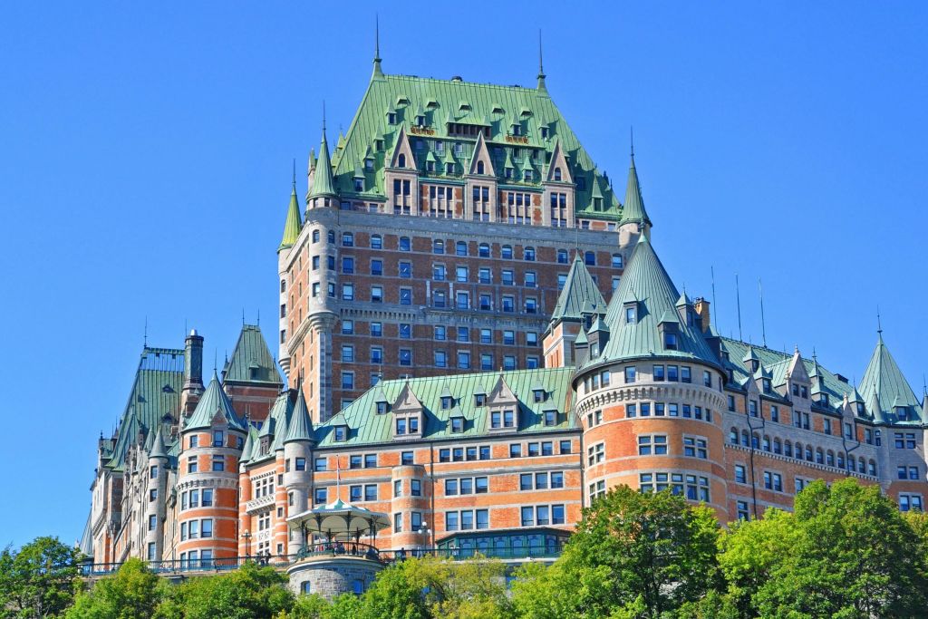 나무로 둘러싸인 맑고 푸른 하늘 아래 녹색 지붕과 붉은 벽돌 벽이 있는 유서 깊은 건물입니다.