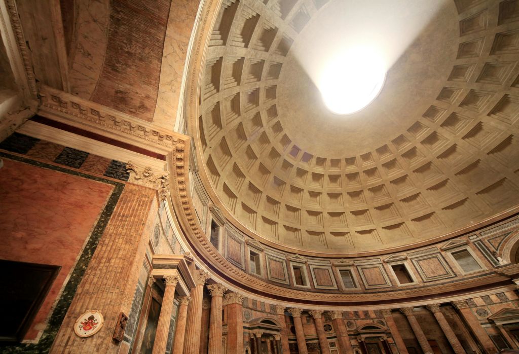 중앙 오큘러스가 있는 판테온 돔의 내부 전경은 아래에 웅장한 콘크리트 천장과 고전적인 기둥을 보여줍니다.