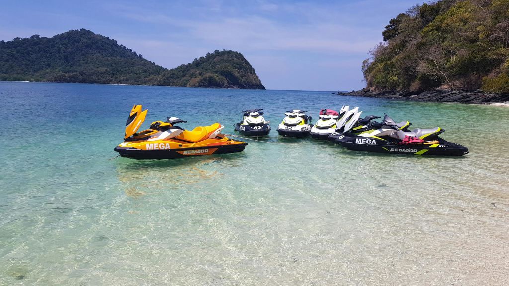 푸른 하늘 아래 언덕이 많은 섬을 배경으로 해변 근처의 맑고 얕은 물에 주차된 제트 스키.