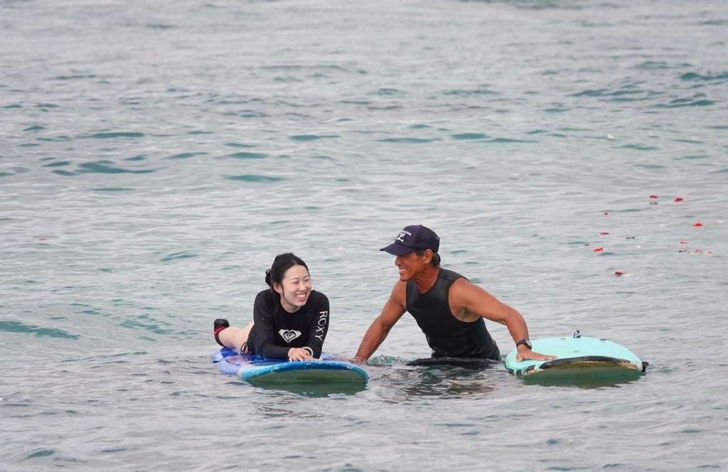 잔잔한 물 위에 떠 있는 서핑보드 위에 잠수복을 입은 두 사람이 미소를 짓고 상호작용하고 있습니다.