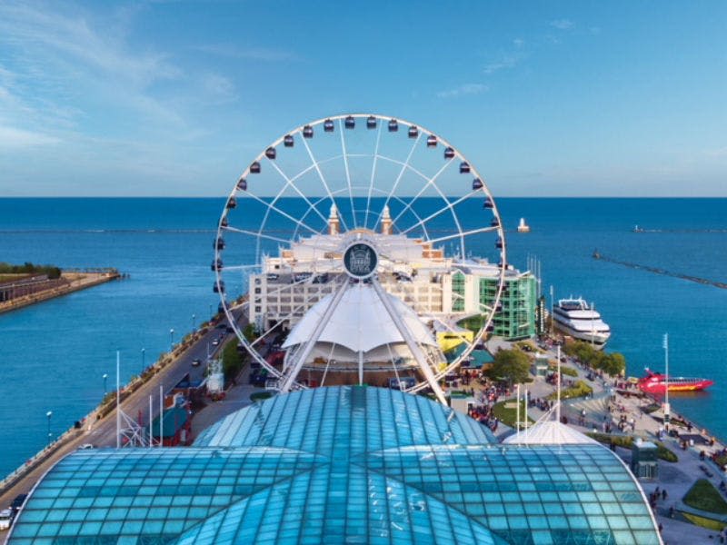 유리 지붕 구조물에서 바라본 수변 건물 근처의 대관람차. 푸른 바다와 하늘을 배경으로.