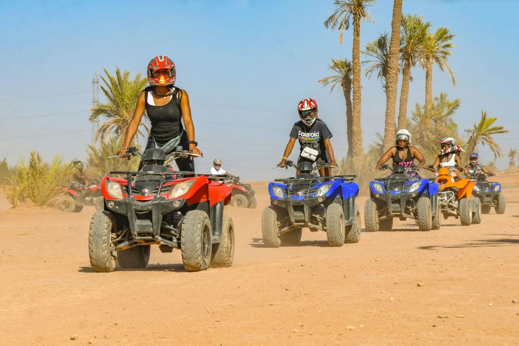 세 사람이 야자수를 배경으로 흙길에서 ATV를 타고 있습니다. ATV 한 대는 빨간색, 두 대는 파란색입니다.