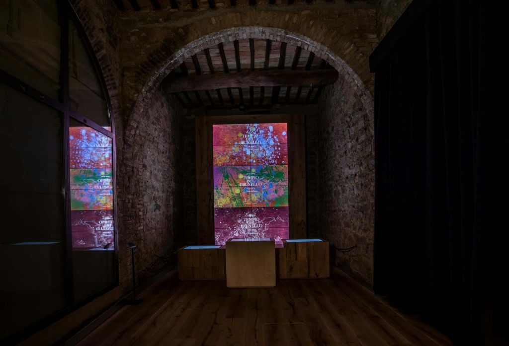 크고 화려한 디지털 디스플레이와 그 아래에 목조 구조물이 있는 석조 벽이 있는 어두운 조명 객실입니다.