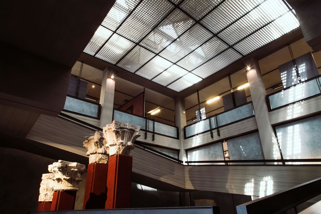 높은 천장, 그리드 패턴의 채광창, 그리스 기둥, 금속 난간이 있는 여러 층의 인테리어.