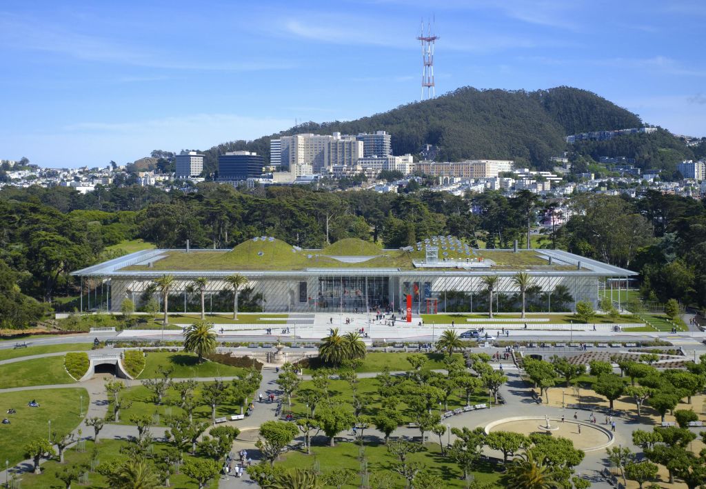 도시 풍경과 언덕을 배경으로 나무로 둘러싸인 공원의 녹색 지붕이 있는 현대적인 건물의 공중 전망.
