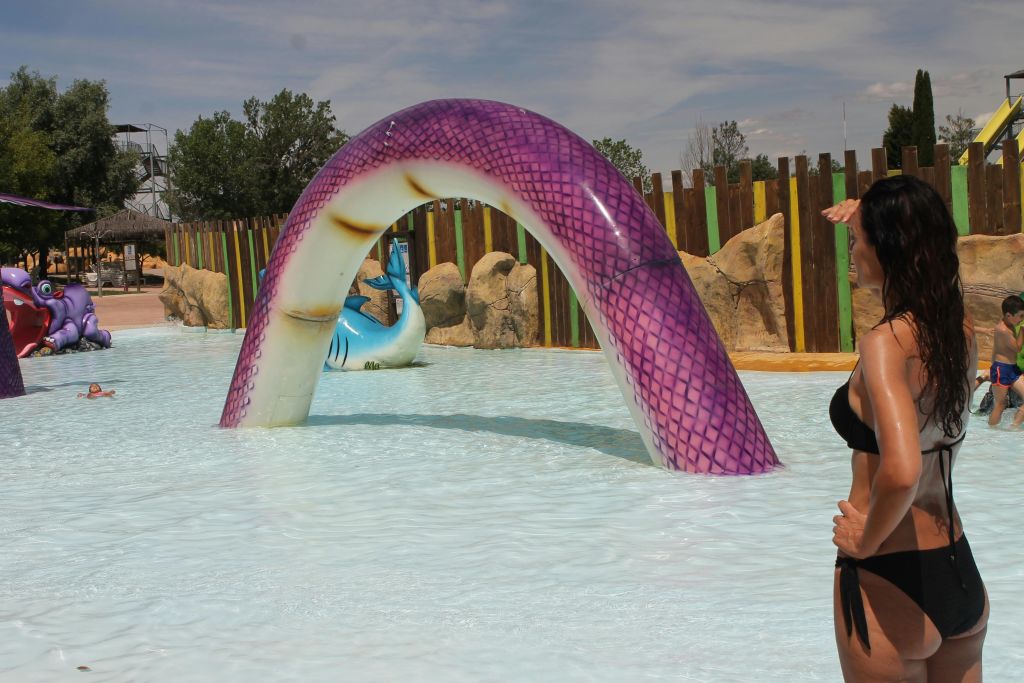 보라색 뱀 미끄럼틀, 나무 울타리, 사람이 수영장의 가장자리를 엿보는 워터파크 장면.