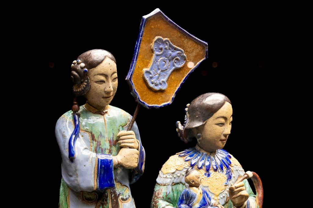 검은색 배경에 방패 모양의 물건을 들고 있는 전통적인 복장의 장식용 세라믹 피규어 두 개.