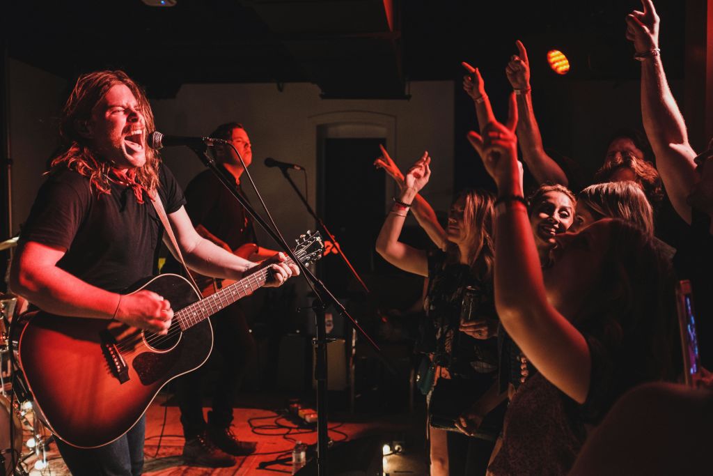 열정적인 관객이 환호하는 동안 밴드와 함께 무대에서 열정적으로 노래하고 기타를 연주하는 뮤지션.