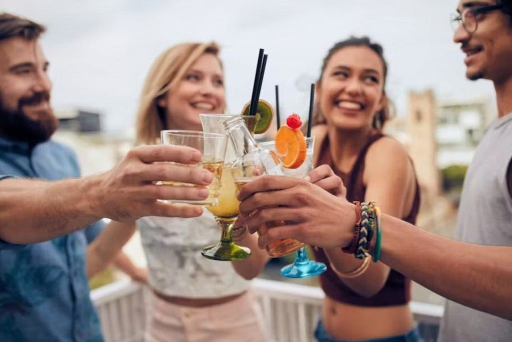 화창한 날 야외에서 과일로 장식된 알록달록한 음료로 가득한 잔에 미소를 짓고 찰칵거리는 세 명의 친구.